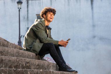 Full length profile portrait smiling young man sitting on steps with mobile phone