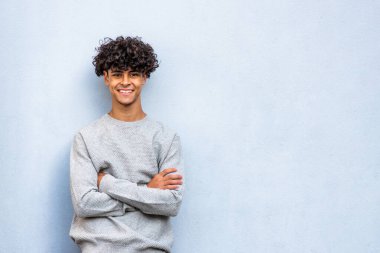 Portrait smiling young North African man with arms crossed by blue background 