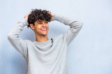 Portrait young handsome North African man smiling with hands in hair by blue background 