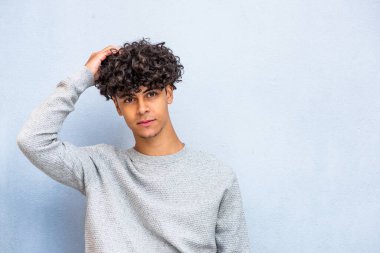 Portrait handsome young North African man posing with hand in hair by blue background 