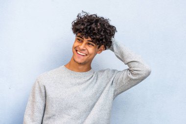 Portrait young man laughing with hand in hair by blue wall 