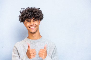 Portrait smiling young North African man with thumbs up hand sign by blue background 