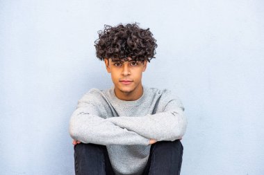 Portrait cool North African guy sitting against blue wall