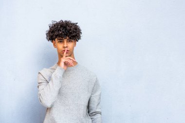 Portrait young North African man with finger over lips against blue background 
