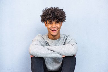 Portrait cool young guy sitting against blue wall and smiling