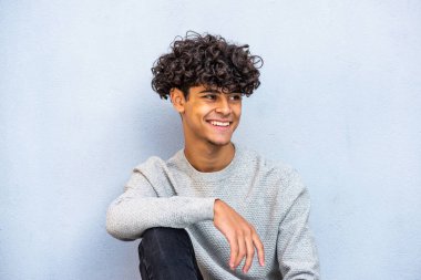 Portrait young guy sitting against blue wall and smiling