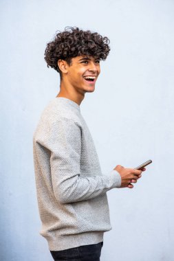 Portrait happy young arabic man holding cellphone by gray background  