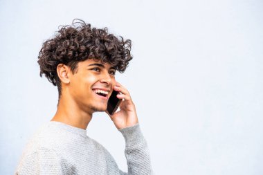 Close up side portrait happy young North African man laughing while talking with cellphone by gray background 