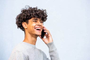 Close up side portrait young North African man laughing while talking with cellphone by gray background 