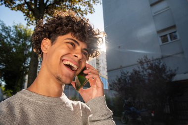 Close up portrait laughing young man talking with cellphone outside
