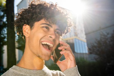 Close up portrait laughing young man talking with mobile phone outside