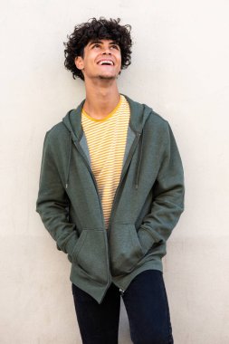 Portrait smiling young man standing by white wall and looking up