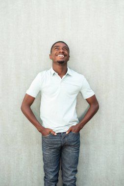 Portrait smiling young African American man standing by wall and looking up