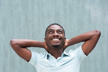 Close up portrait happy young African American man smiling with hands behind head and looking up