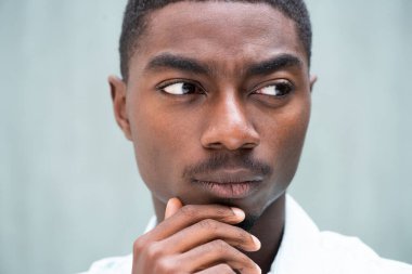Close up portrait serious young African American man thinking with hand to chin glancing away