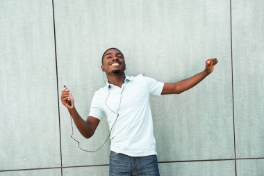 Portrait happy young African American man listening to music with earbuds and mobile phone 