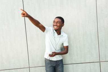 Portrait happy young black man holding cellphone listening to music and pointing