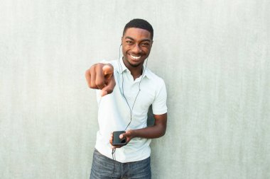 Portrait laughing young black man with cellphone and earbuds pointing finger