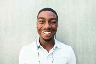 Close up front portrait smiling young African American man listening to music with earbuds 