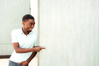 Portrait happy young African American man leaning against wall and pointing finger to empty space