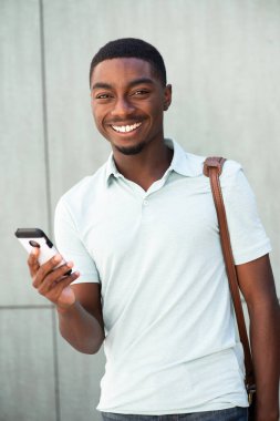 Portrait smiling young african American man holding mobile phone and bag