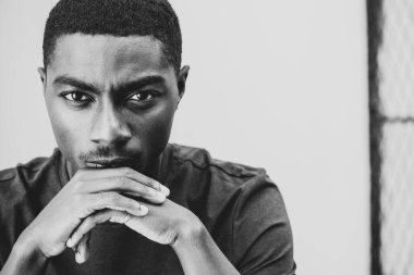 Close up black and white portrait handsome young black man resting chin on hands 