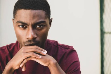 Close up portrait handsome young African American man resting chin on hands 