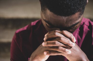 Close up portrait young black man with head in resting in clasp hands 