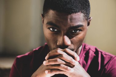 Close up portrait young black man staring with hands clasp 