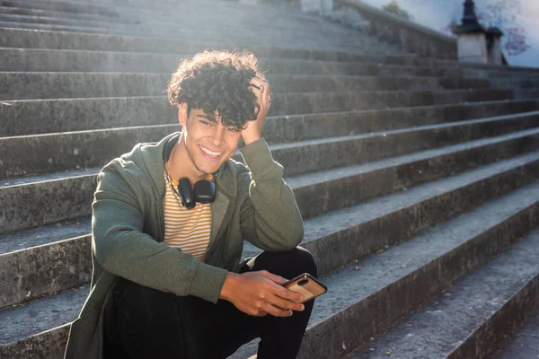 Portrait Smiling Young Man Man Sitting Steps Mobile Phone Headphones — Stockfoto