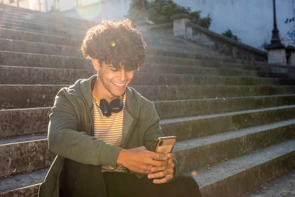 Portrait happy young guy sitting on steps outside with mobile phone