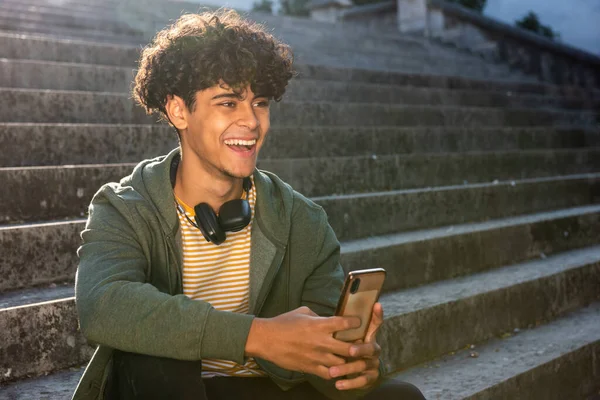 Portrait laughing young man sitting on steps with cellphone