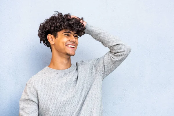 Close up portrait happy young North African man smiling with hand in hair by blue background 