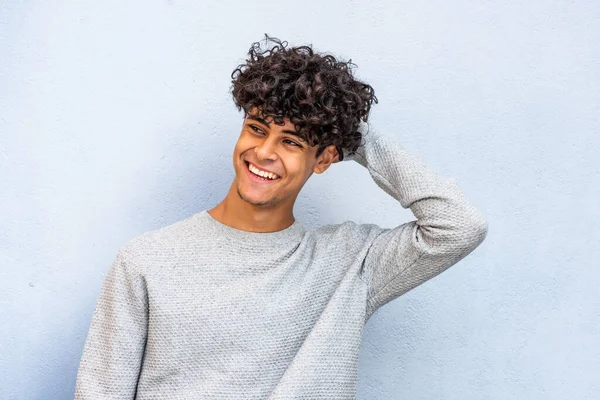 Portrait young man laughing with hand in hair by blue wall 