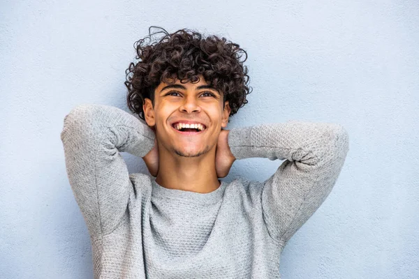 Close up portrait young North African man laughing with hands behind head by blue background