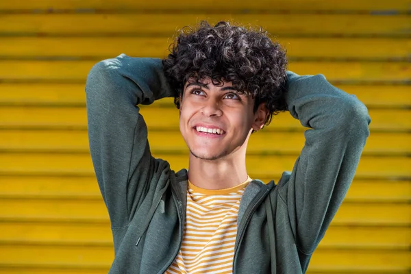 Close up portrait happy young arabic man with with hands behind head and looking up by yellow background 