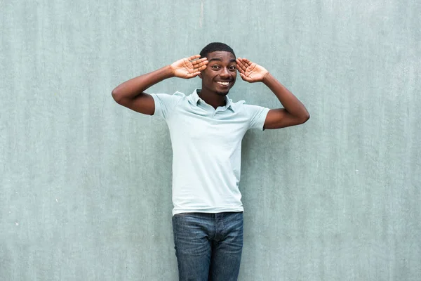 Portrait smiling young black man with hands to face by blue wall