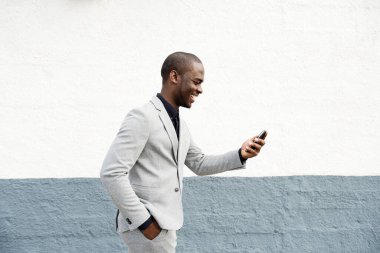 Duvarda telefonla yürüyen mutlu Afro-Amerikan iş adamının portresi.