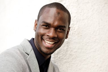 Beyaz duvarda gülümseyen yakışıklı Afrikalı adamın yakın portresi.