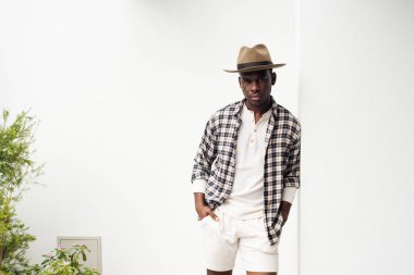 Duvara yaslanmış şapkalı havalı Afrikalı Amerikalı adamın portresi.