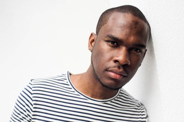 Beyaz duvara yaslanmış yakışıklı zenci portreyi yakından çek. 