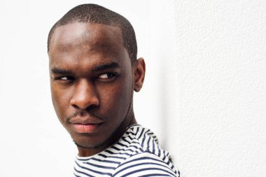 Beyaz duvara yaslanmış ciddi bir Afro-Amerikan portresi. 