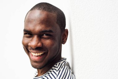 Beyaz arka plana yaslanmış, gülen siyah bir adam.