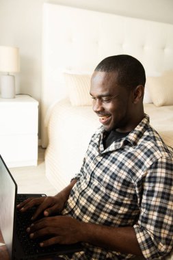Portre Afro-Amerikan adam evde dizüstü bilgisayarla oturuyor.