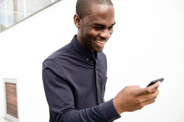 Porträtt Afroamerikansk Man Skrattar Och Tittar Mobiltelefon Vid Vit Vägg — Stockfoto