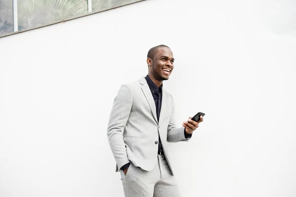Портрет Улыбающегося Афроамериканского Бизнесмена Прислонившегося Белой Стене Мобильным Телефоном — стоковое фото