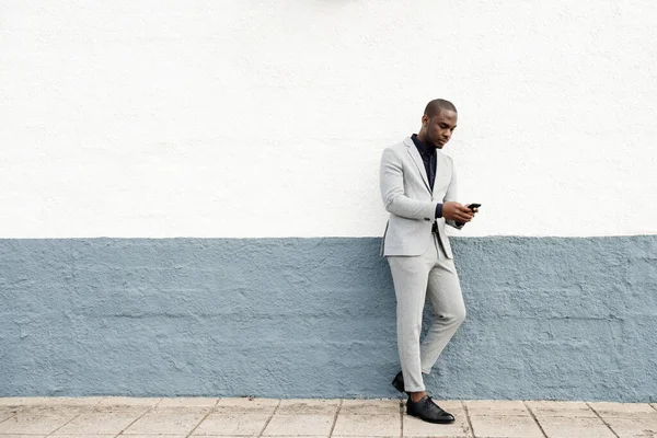 携帯電話で通りによって壁にもたれている深刻なアフリカ系アメリカ人ビジネスマンの完全な体の肖像画 — ストック写真