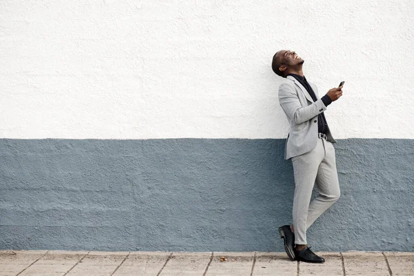 笑着的非洲裔美国商人拿着手机靠墙的全身画像 — 图库照片