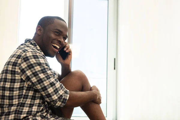 ポートレート笑うアフリカ系アメリカ人男性自宅で携帯電話と話して座って — ストック写真