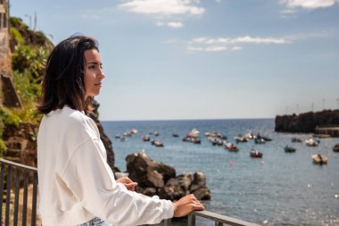 Balkondan denize bakan genç bir kadının portresi.